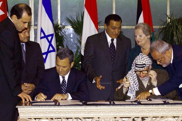 Palestinian leader Yasser Arafat, seated right, consults with Saeb Erekat, right, as Israeli Prime Minister Ehud Barak, seated left, sign the Sharm El-Sheikh Memorandum in 1999.