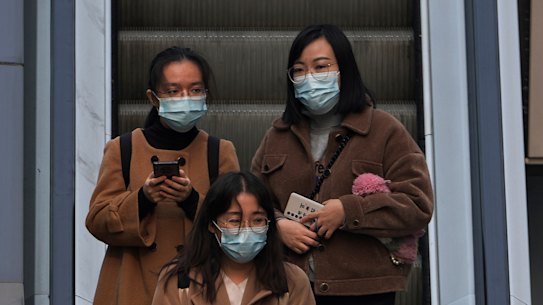 People wearing face masks to protect from COVID-19 take an escalator at a commercial office building in Beijing, on Sunday, November 28.