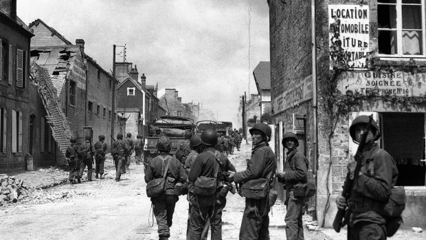 American paratroops patrol in the streets of Sainte-Mere-Eglise, France, before pushing on toward Cherbourg.  June 1944.