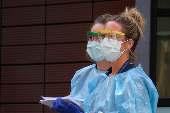 Hospital staff assist people waiting in line to be screened for COVID-19 outside the Royal Melbourne Hospital. Around 80 members of Victoria's health workforce have tested positive to coronavirus.