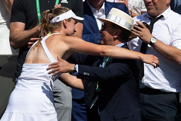 Elena Rybakina holding the Australian Open trophy on stage, smiling with her team in the background at Melbourne Park.