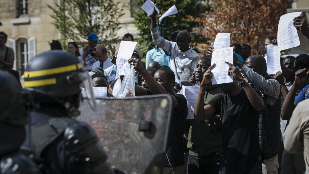 Migrants shouts hold up papers with a list of their demands and shout at police outside the Pantheon in Paris.