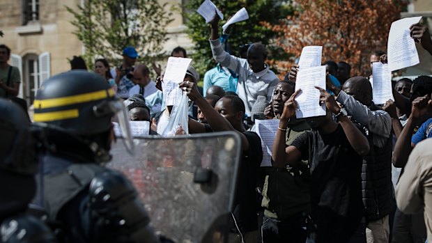 Migrants shouts hold up papers with a list of their demands and shout at police outside the Pantheon in Paris.