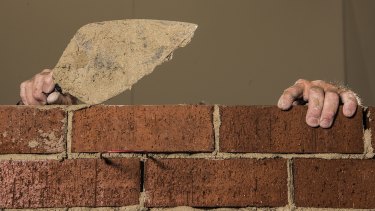 Artist Mitch Cairns building a red brick wall.