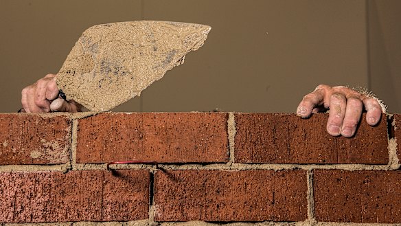 Artist Mitch Cairns building a red brick wall.
