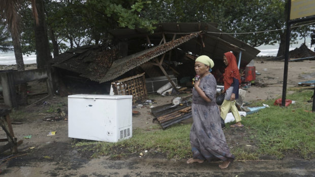 Residents walk past a house damaged by a tsunami, in Carita, Indonesia.