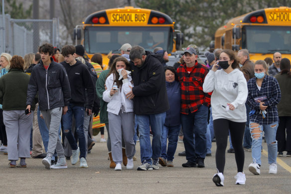 Parents walk away with their kids from the Meijer’s parking lot, where many students gathered following the mass shooting at Oxford High School.