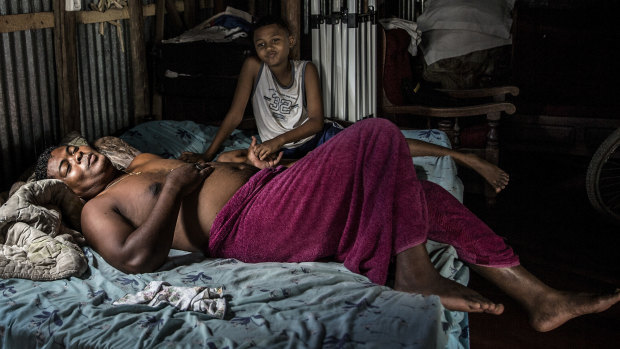 Pascale Rasafindakoto, a “commisionnaire”, or middleman, lies at home in bed with his son, in Sambava, Madagascar.