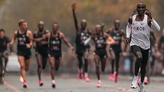 Eliud Kipchoge approaches the finish line, with his pacemakers celebrating behind. 