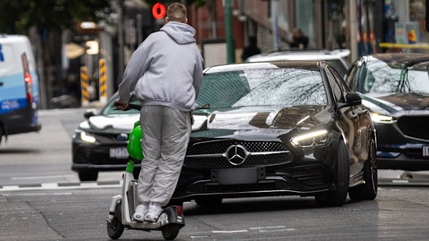 A man rides an e-scooter the wrong way down Little Bourke Street with no helmet in 2024, swerving to miss an oncoming car. 
