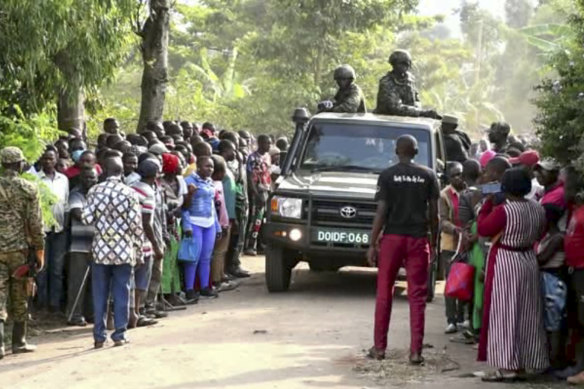 Security forces drive past a crowd of people gathered outside the Lhubiriha Secondary School following an attack on the school near the border with Congo, in Mpondwe, Uganda.