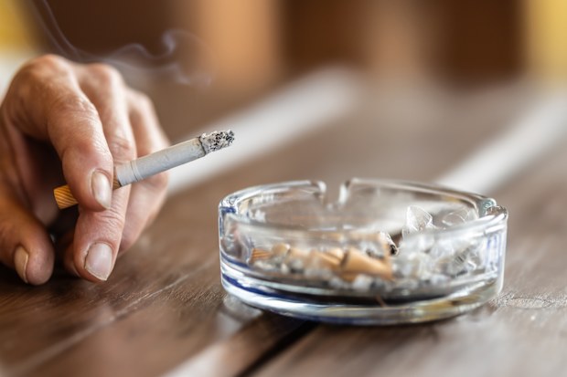 Stock image of a woman smoking and tapping cigarette ash into an ashtray.