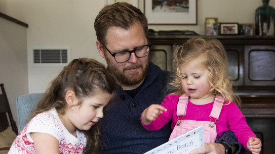 Andrew Kennedy at home, reading to daughters Isla, 5, and Hope, 2.