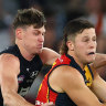 Jake Soligo of the Crows handballs whilst being tackled by Sam Walsh of the Blues.