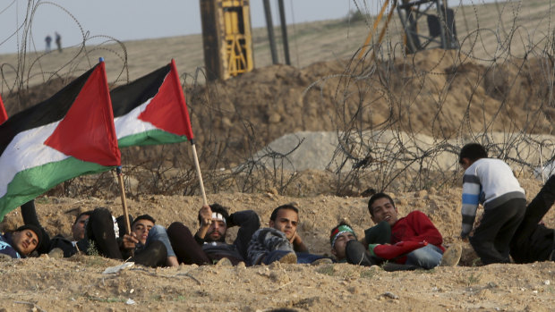 Protesters take cover while waving their national flags near the fence of Gaza Strip border with Israel during a protest east of Gaza City, on Friday.