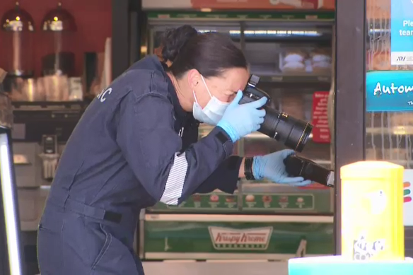 A forensic officer takes photographs of the scene at the 7-Eleven store. 