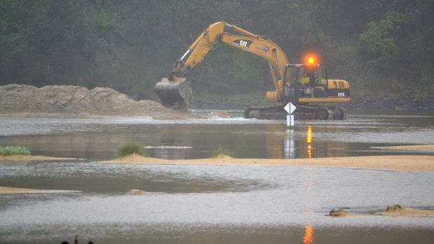 An excavator begins to dig out a channel in the sandbar blocking off Lake Conjola from the ocean on December18, 2018.