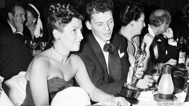 At a crowded table at Ciro\'s, Frank Sinatra steals a glance at his Oscar which he won for his performance in the film "The House I Live In," as his wife Nancy looks on in 1946.