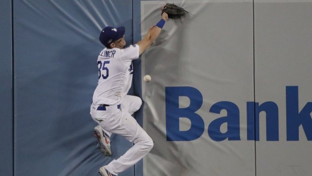 Cody Bellinger crashes into the wall in centre field as he attempts a catch against the Brewers.