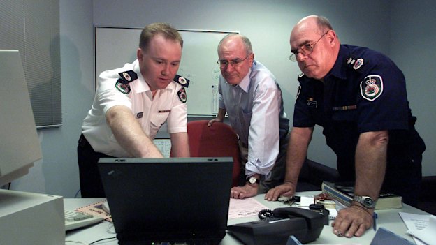 Then prime minister John Howard is briefed by Shane Fitzsimmons and Phil Koperberg of the RFS before visiting the bushfire devastated suburb of Warragamba in 2001.