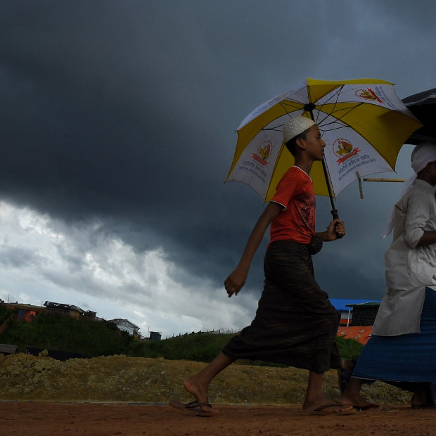 Storm clouds hang overhead as a Rohingya boys carrying umbrellas walk on a main road in Kutupalong camp.