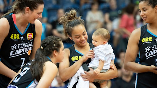 The Canberra Capitals' Lauren Scherf, Abby Cubillo, and Hannah Young share the moment with Leilani Mitchell's son Kash after winning the 2018-19 WNBL championship.
