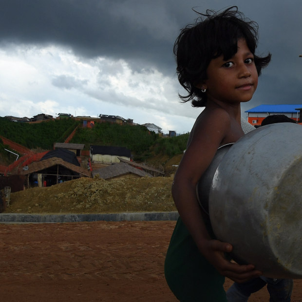 Storm clouds hang overhead as a Rohingya child carries a pot in Kutupalong camp.