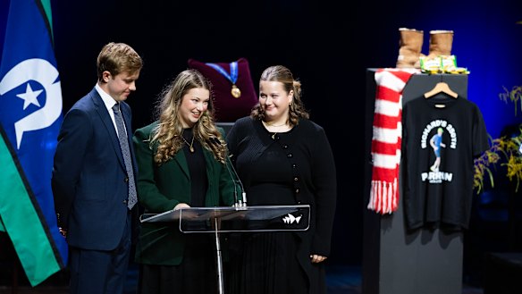 Surrounded on stage by items from his life, Richard Scolyer’s children – Matthew, 20, Emily, 22, and Lucy, 18 – deliver a joint eulogy at the service.
