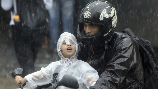 A boy rides a bike wrapped in a raincoat in Mumbai, India, where a building has collapsed.