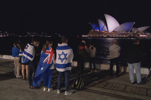 Supporters watch the Sydney Opera House lit up in blue and white.