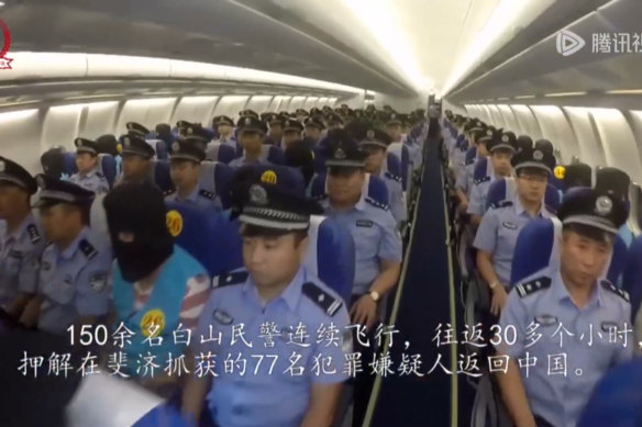 Hooded suspects, whom Chinese police accuse of suspected cyber scams, sit between Chinese police officers on a charter plane from Fiji to China in 2017.