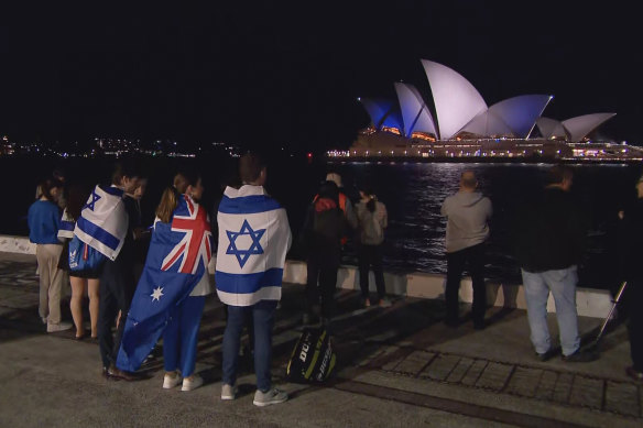 Supporters of Israel watch the Sydney Opera House lit up in blue and white.