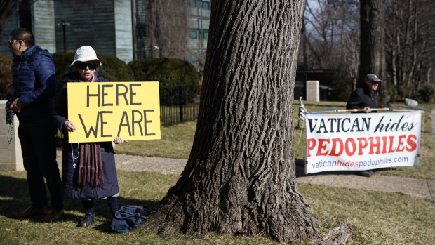 A group with Catholic Laity for Orthodox Bishops and Reform, left of the tree, gathers to pray the rosary, as John Wojnowski holds a sign at right outside the Apostolic Nunciature of the Holy See in Washington.