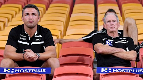 Rugby league in the coronavirus age: Souths’ Sam Burgess, Jason Demetriou and Wayne Bennett swap the coaches’ box for the grandstand at Suncorp Stadium on Friday night.