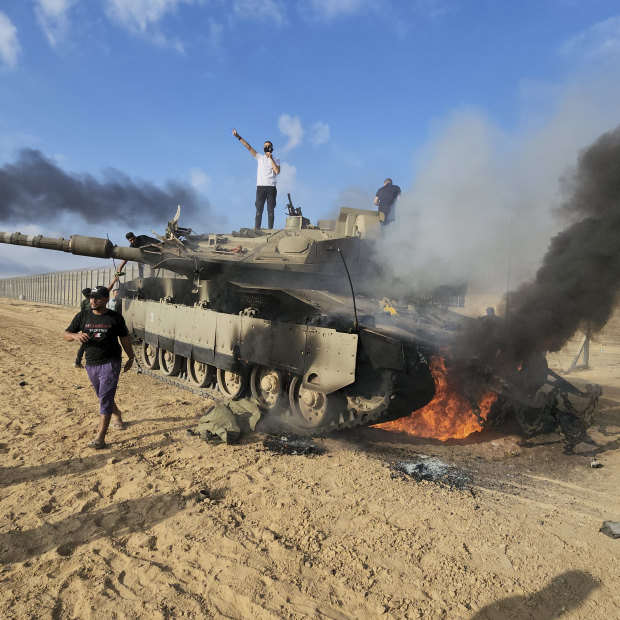 Palestinians celebrate by a destroyed Israeli tank at the Gaza Strip fence east of Khan Younis on October 7. 