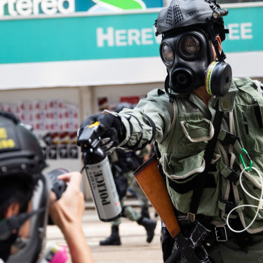 A riot police officer aims pepper spray at a journalist covering a protest in September 2019. 