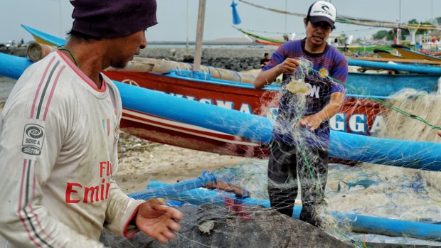 Taufik a fisherman from Kedonganan, Bali cleaning and untangling plastic trash caught on his fishing net. 