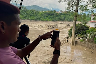 People take photos and videos of the swollen, debris-choked banks of the Trishuli River.