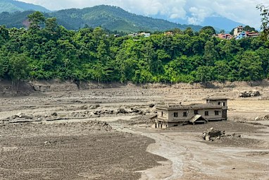 A damaged house stands precariously near the swollen, debris-choked banks of the Trishuli River.