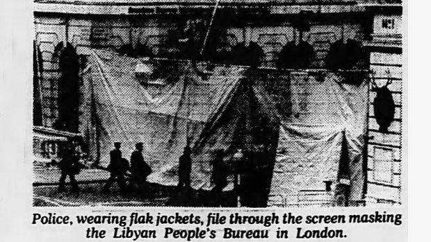 Police, wearing flak jackets, file through the screen masking the Libyan People's Bureau in London - Clipped from The Age.