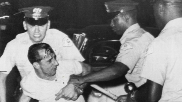 Despite a bloodied head, a white demonstrator grapples with police after fights broke out between black and white people when three black families moved into a predominantly white Chicago suburb in 1963. 