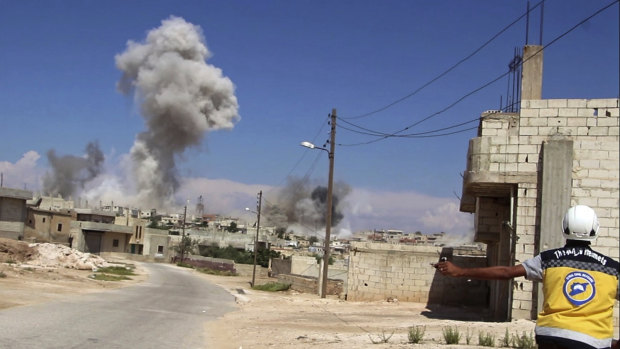 A civil defense worker watches as smoke rises from a Syrian government airstrike, in Hobeit village, near Idlib.