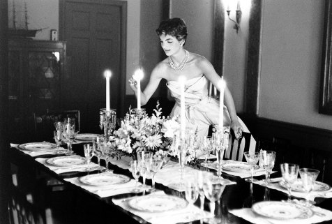 Newlywed Jackie Kennedy, dressed to the nines, lights candles for a dinner party. 