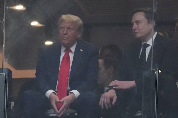 Donald Trump with Elon Musk in a box suite behind a bulletproof shield.