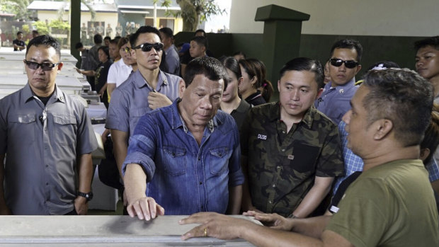 Philippine President Rodrigo Duterte, centre, touches one of the coffinss of victims of last Sunday's bombings of a Roman Catholic Cathedral on Jolo. 