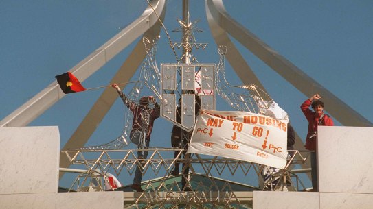 Protestors place flags on the Australian coat-of-arms at the front of Parliament House
