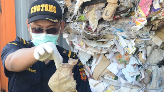 Indonesian Customs official Dhion Priharyanto holds up a used nappy, soft drink containers and a plastic of organic raspberries mixed in with paper that was supposed to be recycled. Instead, it will be sent back to Australia.