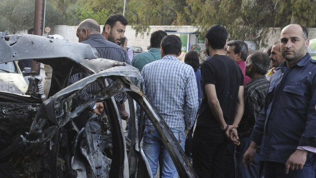This photo released by the Syrian official news agency SANA, shows Syrians gathered next to a bunt car hit by a shelling by members of the Army of Islam rebel group at Rabwa neighborhood in Damascus, Syria, on Friday.
