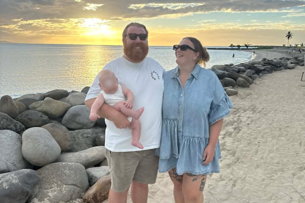 Man, woman and baby standing on a beach at sunset
