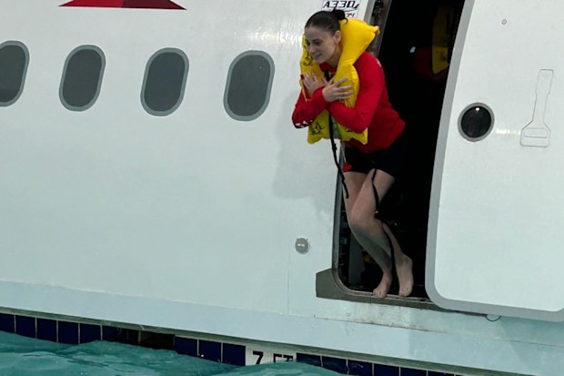 A flight attendant wearing a life jacket jumps from a fake plane door into a pool